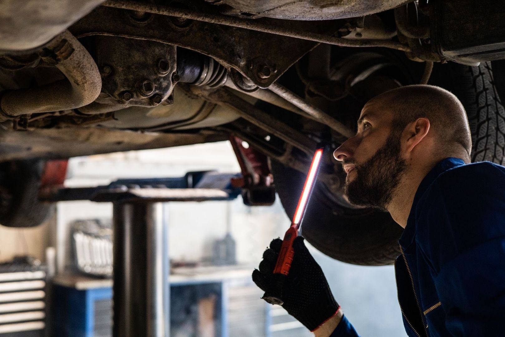 Mechanic Inspecting Rust And Components Beneath A Raised Vehicle