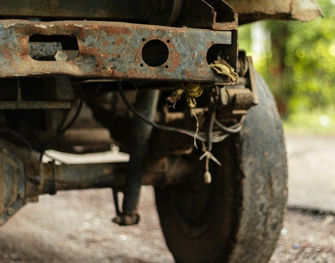 Close-up of rust-covered car underbody frame, tire, and loose wiring